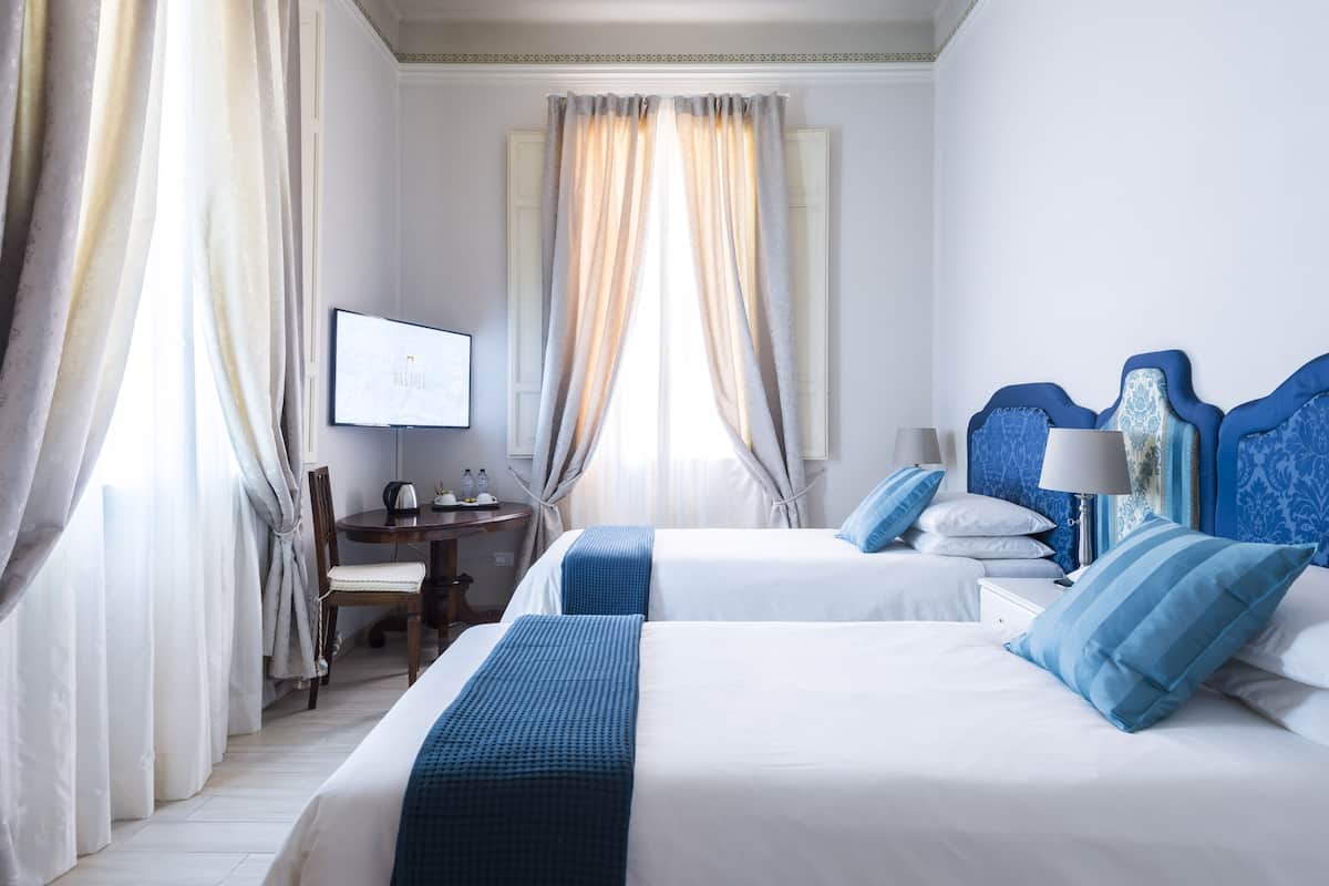 A hotel room with two beds, a desk, a chair, and a television.