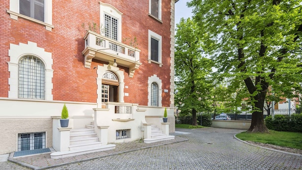 A red brick building with a white facade, a central entrance with steps, and a tree to the right. - Villa Savioli (Bologna)