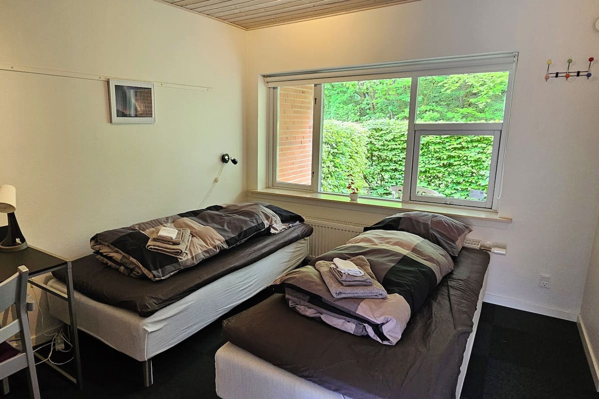 A small, simple room with two single beds, a desk, and a window with a view of greenery.
