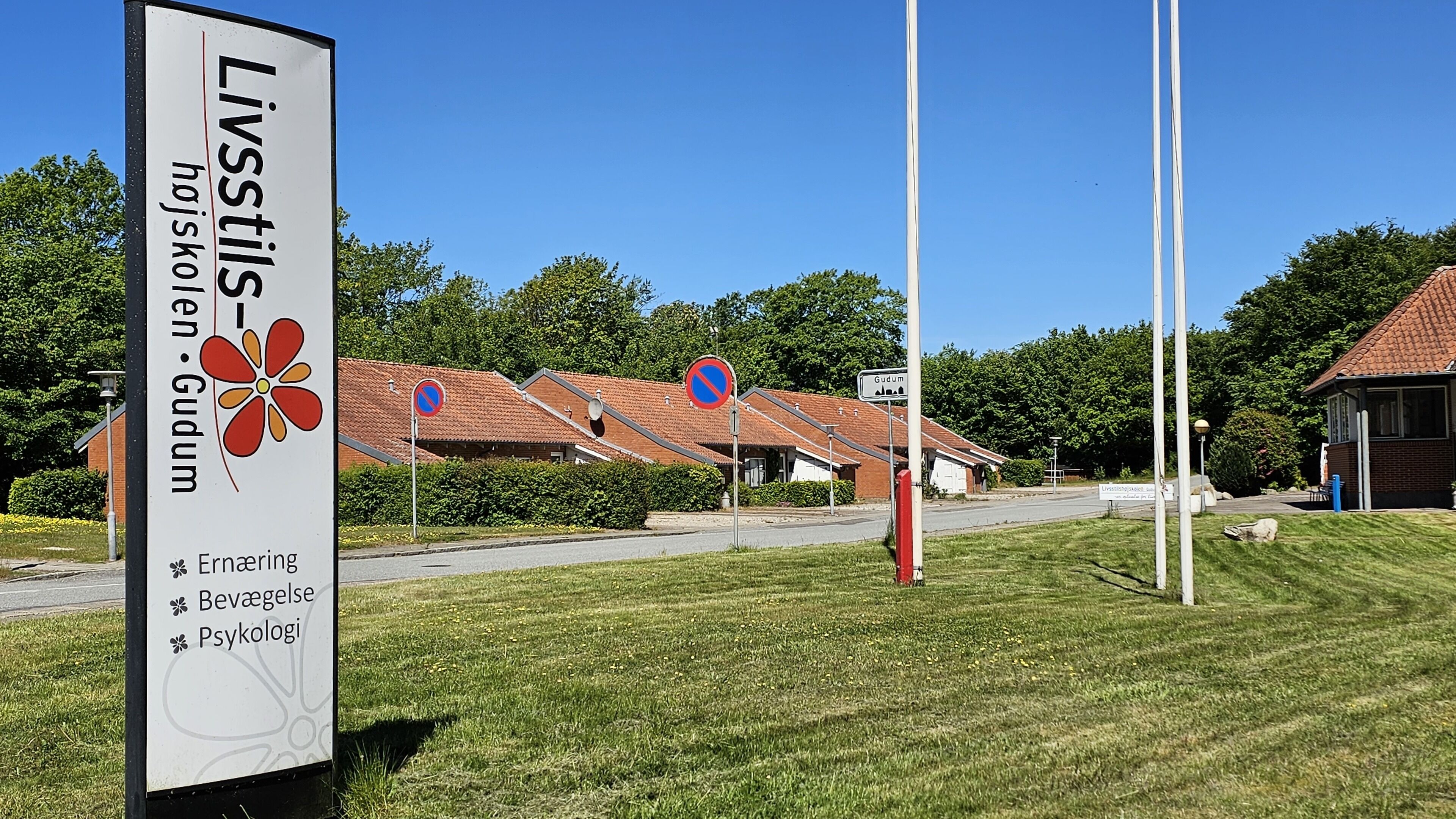 Señal para Livstilstiljen - Håskølen Gudum con diseño floral, que indica un lugar con servicios como sauna, restaurante y psicólogo.
