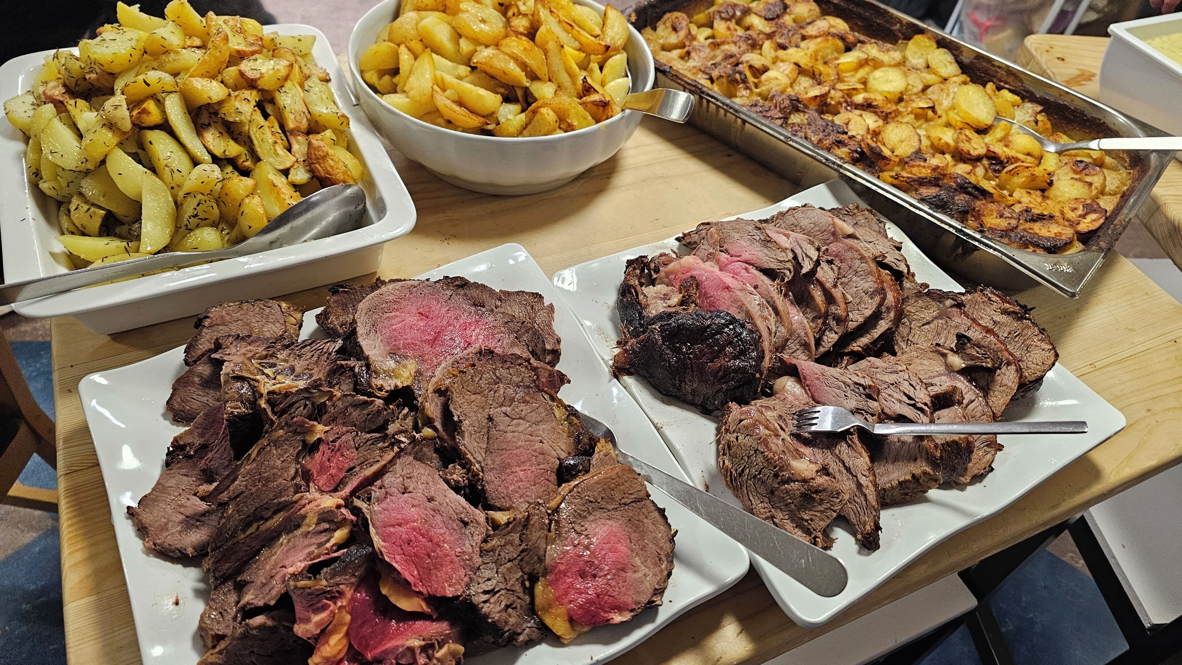 A buffet table with various dishes including sliced beef, roasted potatoes, and a tray of meat.