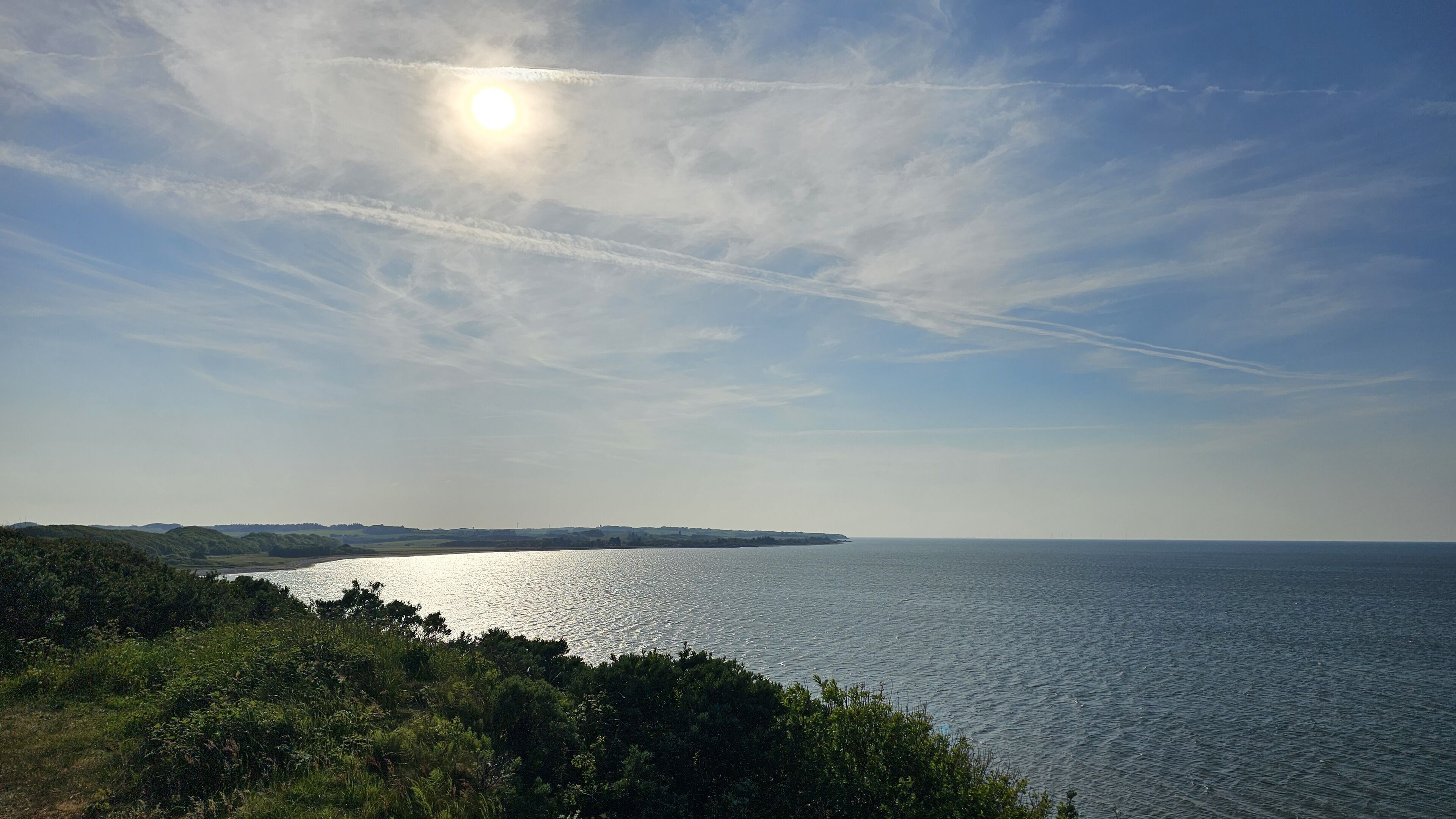 A coastal landscape with a clear sky, a calm sea, and distant land.