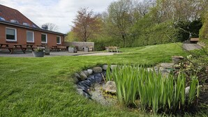 A brick building with a sloped roof, picnic tables, and a grassy area with a small stream. - Gudum Park (Lemvig)