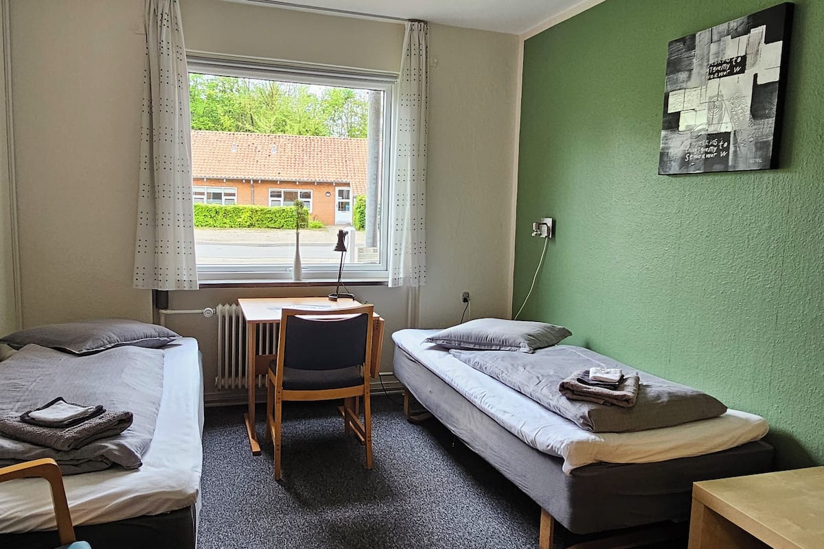 A small, tidy room with two single beds, a desk, and a chair.