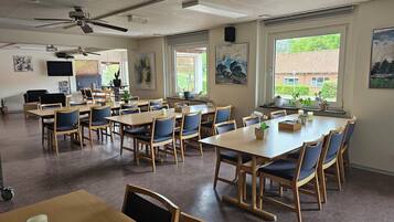 A spacious room with multiple tables and chairs, ceiling fans, and large windows offering views of the outside.