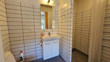 Un baño con paredes de azulejos blancos, un lavamanos y un espejo.