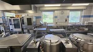 A commercial kitchen with stainless steel appliances, including ovens and a large industrial mixer. - Gudum Park (Lemvig)