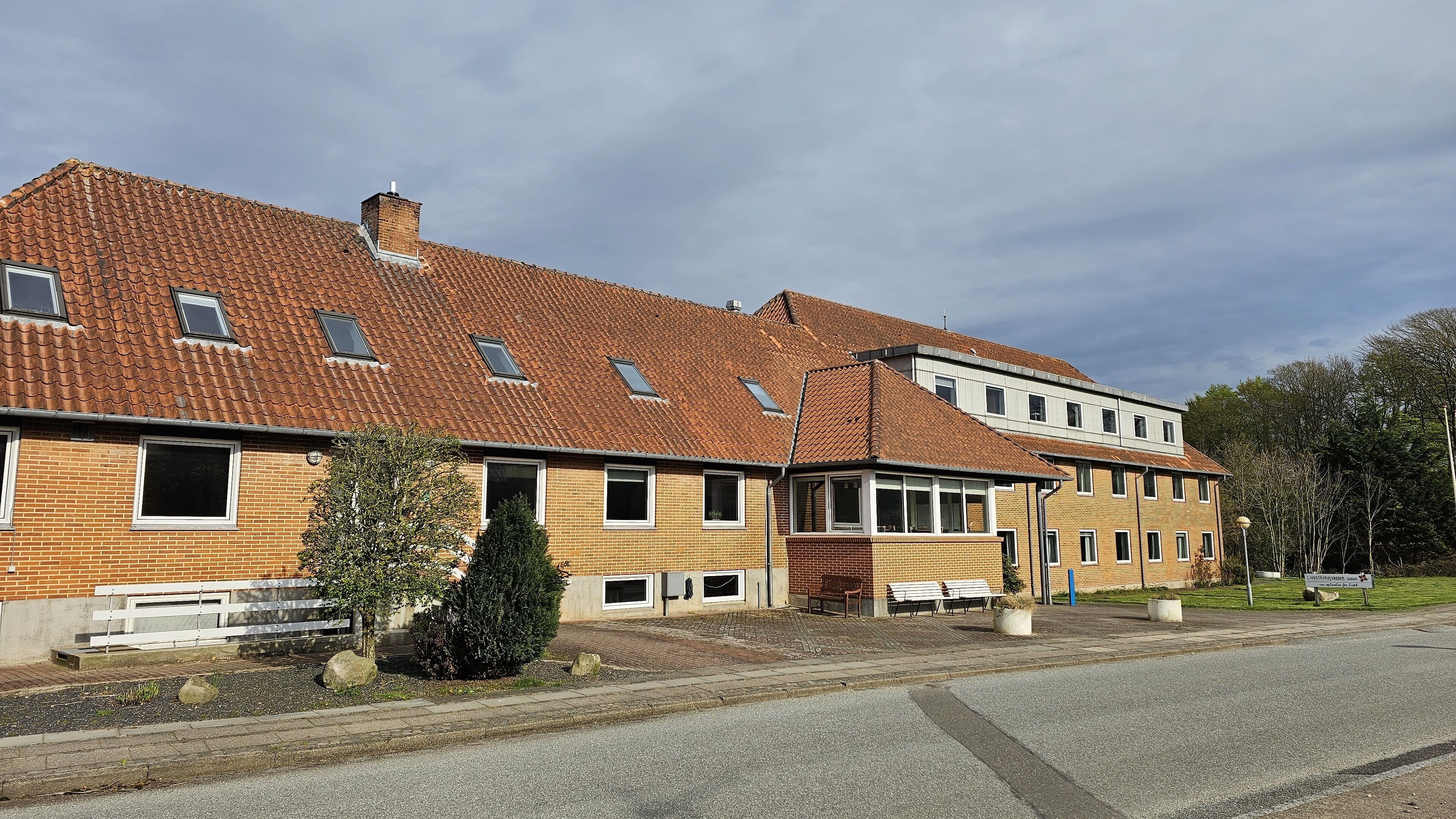 A two-story building with a red-tiled roof, multiple windows, and a paved driveway.