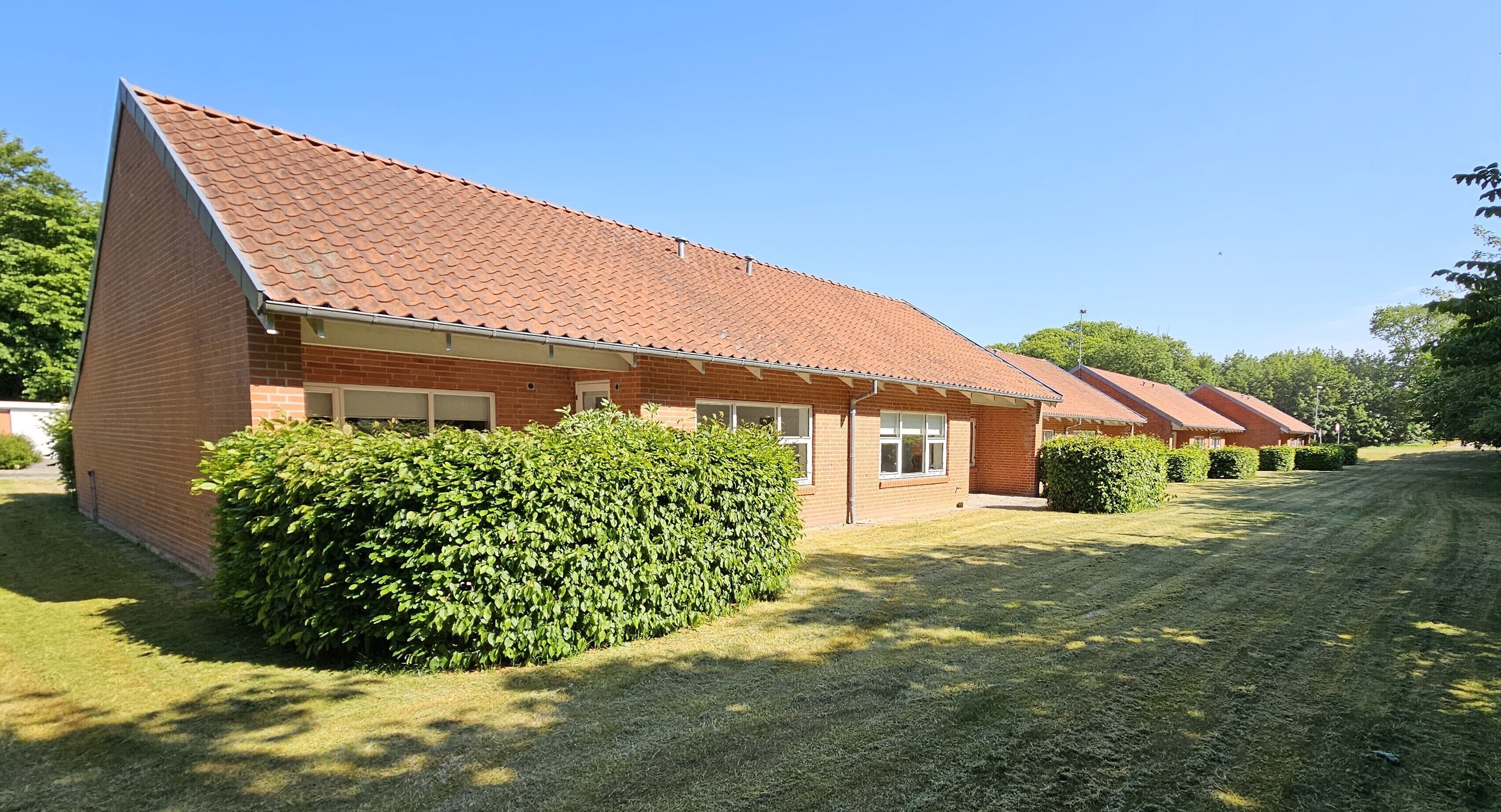 A row of brick buildings with red-tiled roofs, neatly trimmed hedges, and a well-maintained lawn.