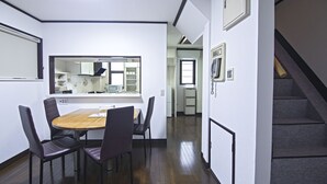 Zona pranzo con tavolo in legno e quattro sedie, cucina sullo sfondo e una scala a destra.