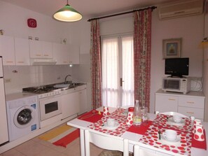 Une cuisine compacte équipée d’un lave-linge, d’une cuisinière, d’un four à micro-ondes et d’une table à manger recouverte d’une nappe rouge et blanche.
