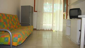 A room with a colorful bed, a television, a cabinet, and a window with curtains. - Holiday apartment mit Terrasse (Bibione)