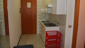 A compact kitchen with a stove, cabinets, and a red basket. - Holiday apartment mit Terrasse (Bibione)
