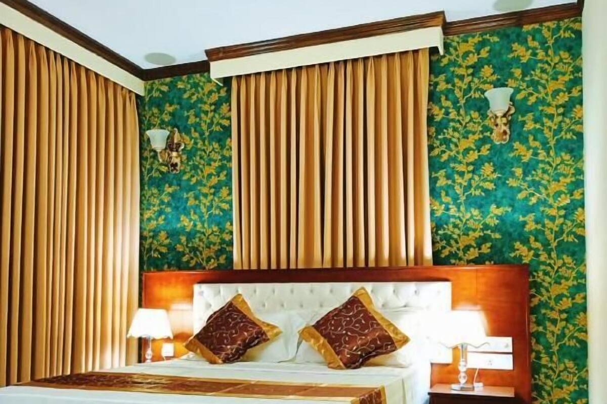 A hotel room with a large bed, two bedside tables, a red carpet, and floral wallpaper.