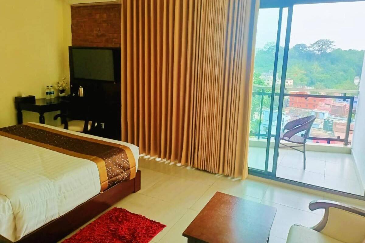 A hotel room with a bed, a desk, a chair, a TV, and a balcony with a view of the city.