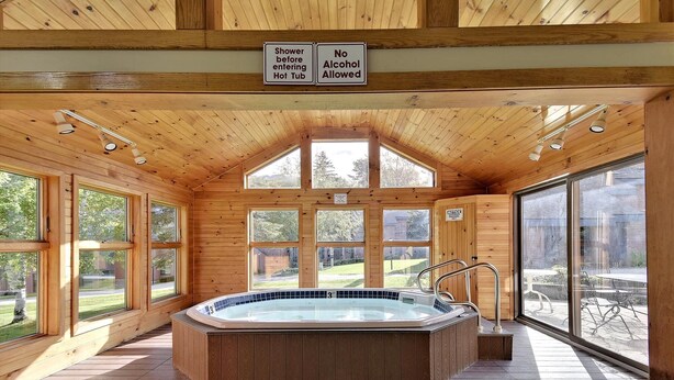 A wooden cabin with a hot tub, large windows, and signs indicating shower before entering and no alcohol allowed.