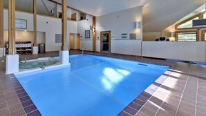 A large indoor swimming pool with a tiled floor and walls, a changing room with a shower, and a reception area with a computer and seating.