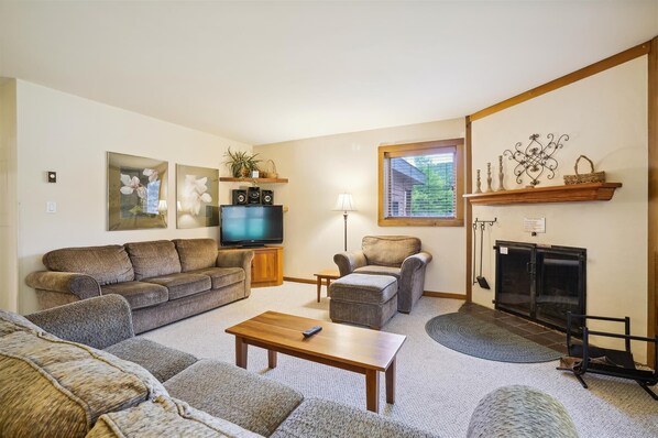 A living room with a sofa, armchairs, a coffee table, a TV, a fireplace, and decorative items on shelves.