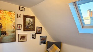A room with a sloped ceiling, a skylight, and a wall adorned with various framed artworks.