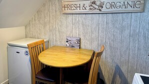 A kitchen with a wooden table and chairs, a small refrigerator, and a 'Fresh & Organic' sign on the wall.