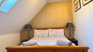 A bedroom with a sloped ceiling, a wooden bed frame, two bedside lamps, and a floral-patterned bedspread.