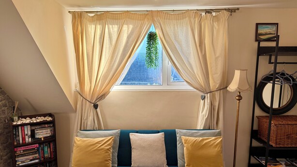 A cozy room with a blue sofa, a bookshelf, a window with curtains, and a lamp.