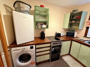 A compact kitchen with a refrigerator, washing machine, stove, microwave, and a small sink.