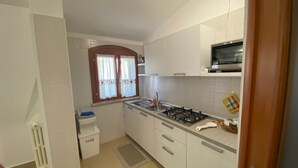 Cocina compacta con armarios blancos, estufa a gas, microondas y una ventana con cortinas.