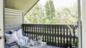 A balcony with a sofa, a table with a plant, and a view of trees and a building. - Staysville - Eiganes (Stavanger)