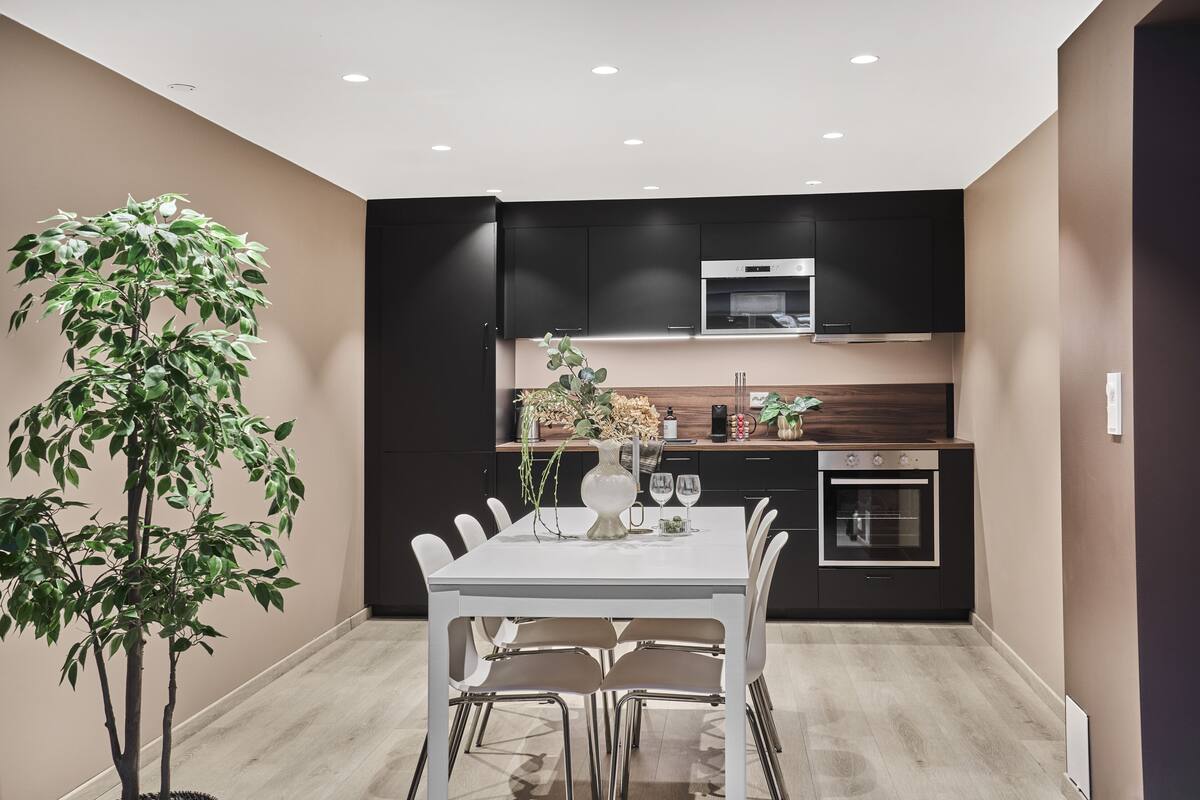 Une cuisine moderne avec des meubles de couleur sombre, une table à manger blanche et une plante en pot.