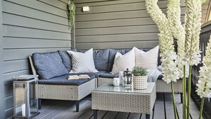 A cozy outdoor seating area with a wicker sofa, a small table, and a lantern. - Staysville - Eiganes (Stavanger)