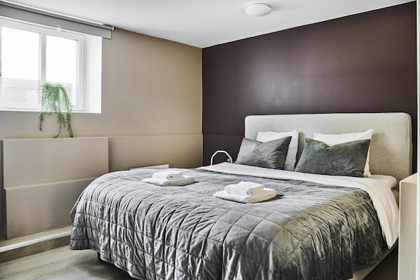 Une chambre moderne avec un lit, une fenêtre agrémentée d’une plante et un mur de couleur sombre.