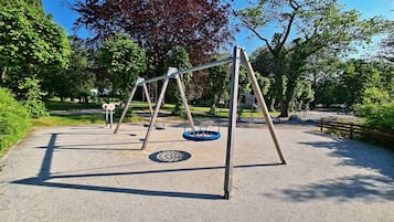 Children can play on the swing set with two swings and a tire swing amidst lush greenery.
