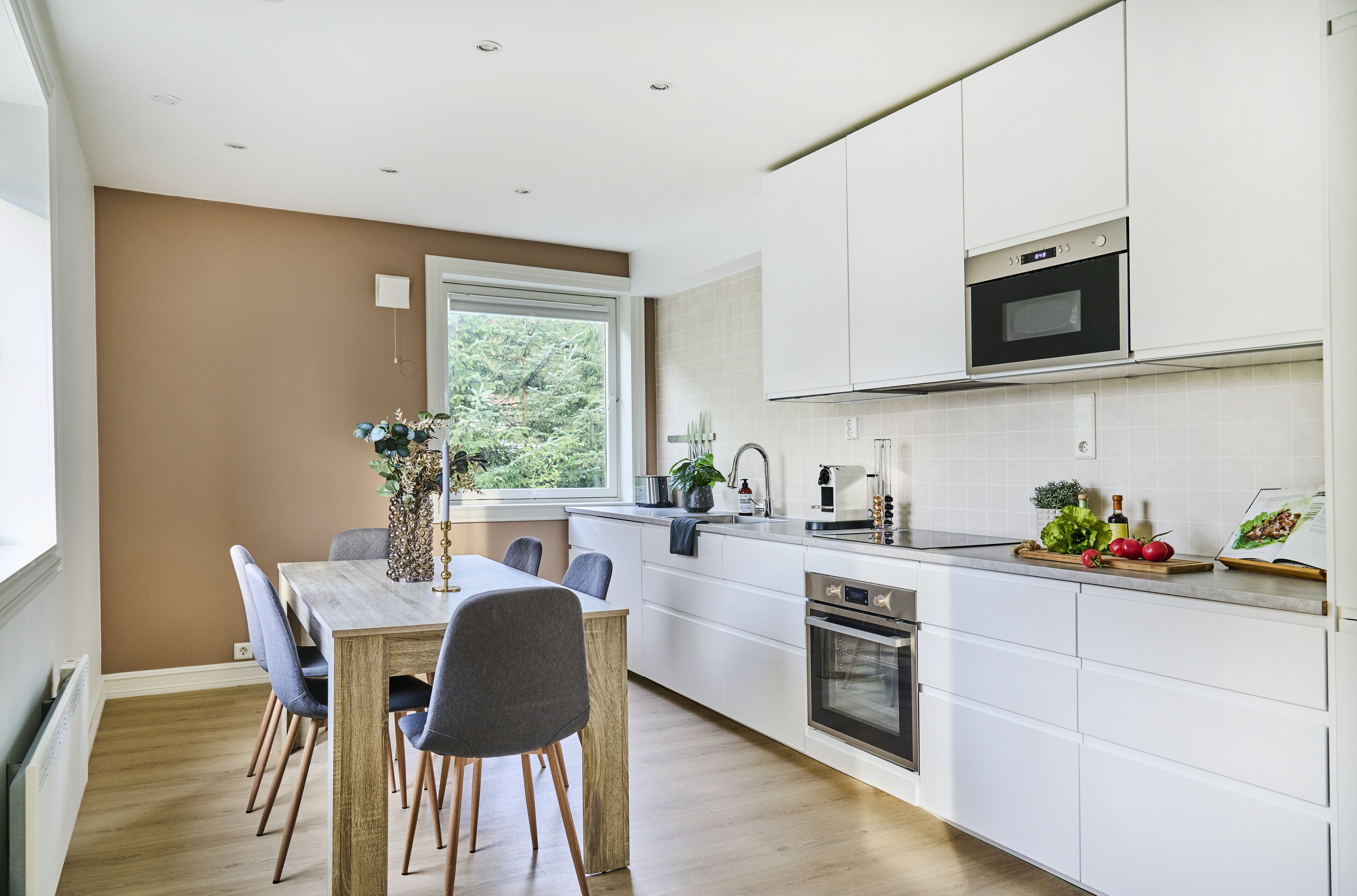 Une cuisine moderne avec des armoires blanches, un four encastré et un coin repas comprenant une table et des chaises en bois.