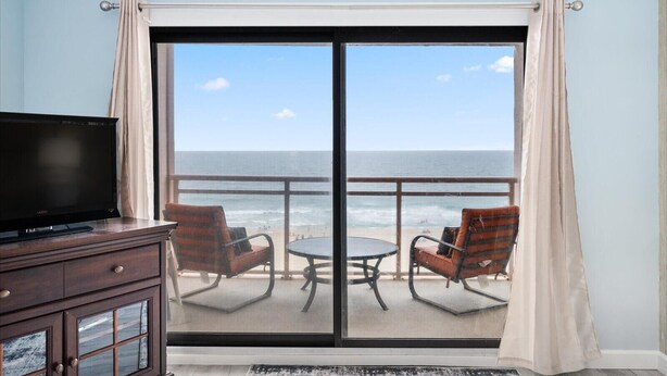 Una habitación con televisión, dos sillones, una mesa y un amplio ventanal corredizo que da a un balcón con vista al océano.