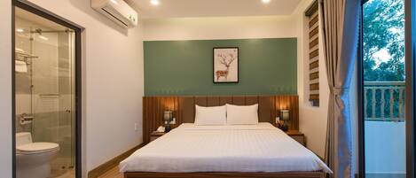 Un hotel moderno con una cama grande, cabina de ducha de vidrio, pared de acento verde y vista al exterior.