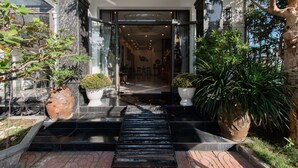 Entrada de hotel de diseño moderno, con puerta de cristal, sendero de piedra y plantas en macetas.