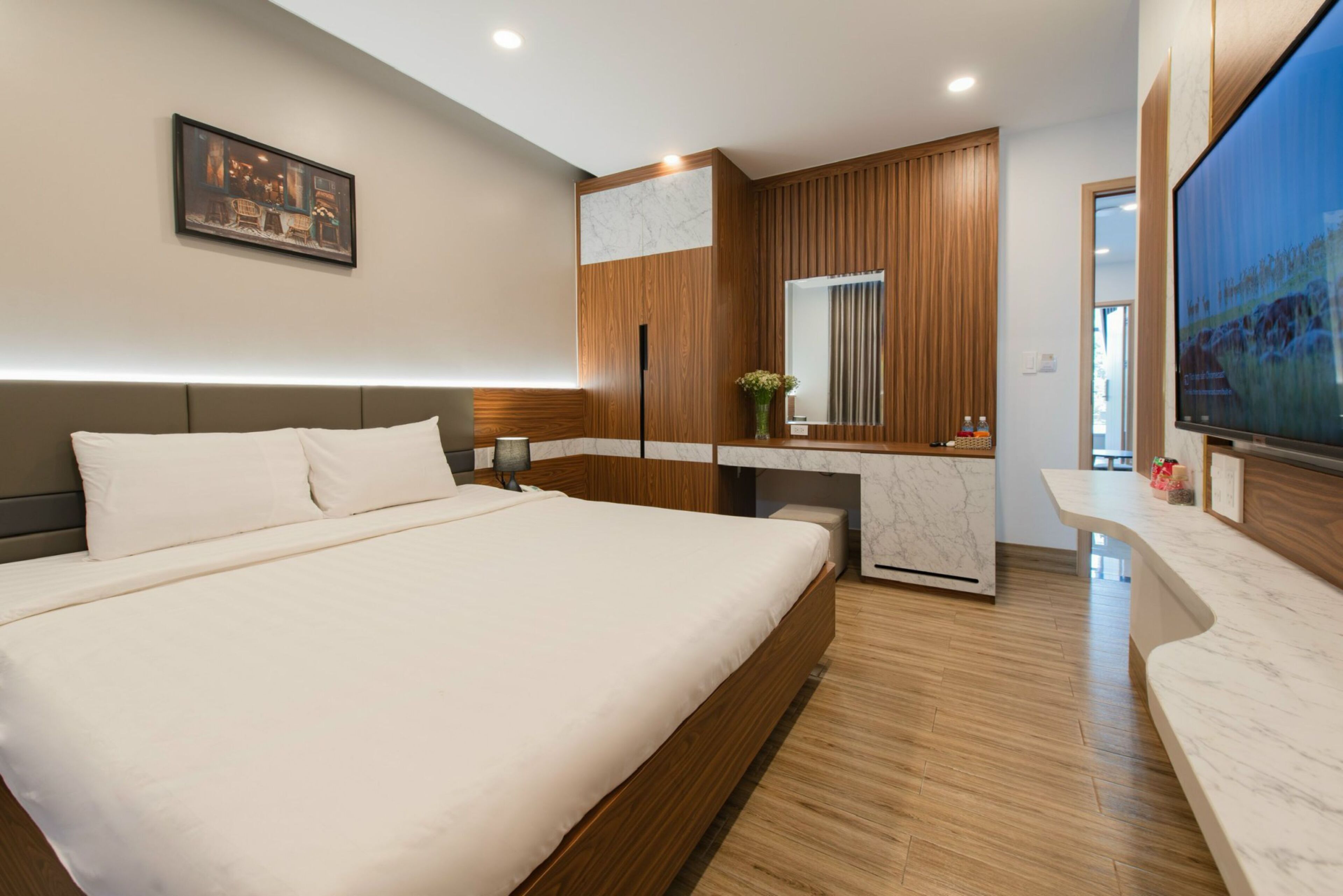Una habitación de hotel moderna con una cama grande, paneles de madera, una pared de acento de mármol, un televisor de pantalla plana y una pequeña zona de escritorio.