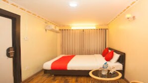 A hotel room with a bed, a round table with a bottle and a glass, and a curtain. - MeroStay 210 Hotel Tone (Kathmandu)