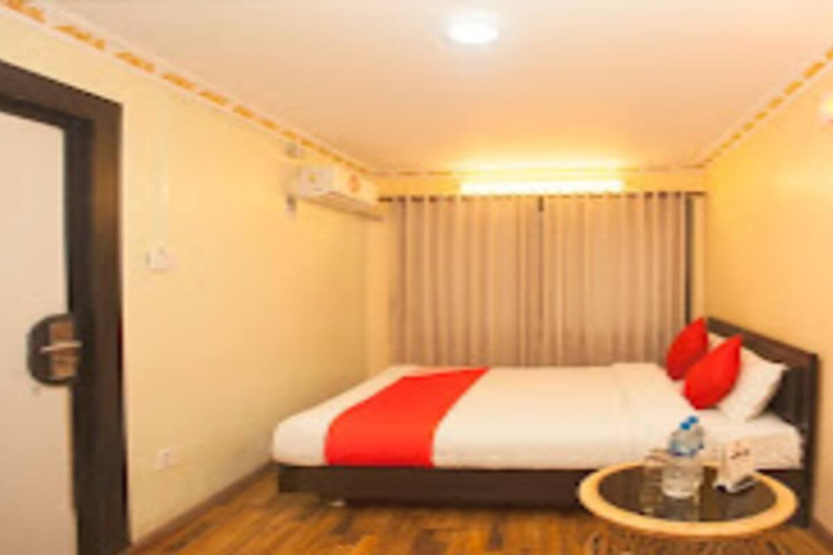 Habitación de hotel con cama, una mesa redonda, una botella y un vaso, además de una cortina.