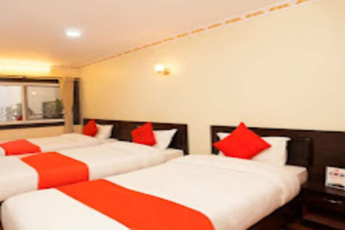 Habitación de hotel con dos camas, cada una con ropa de cama blanca y detalles rojos, cabecero de madera y mesita de noche con lámpara.
