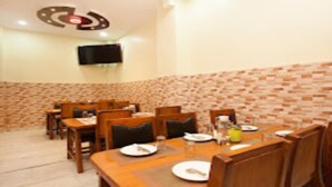 A dining area with a brick-patterned wall, wooden tables and chairs, and a flat-screen TV mounted on the wall. - MeroStay 210 Hotel Tone (Kathmandu)