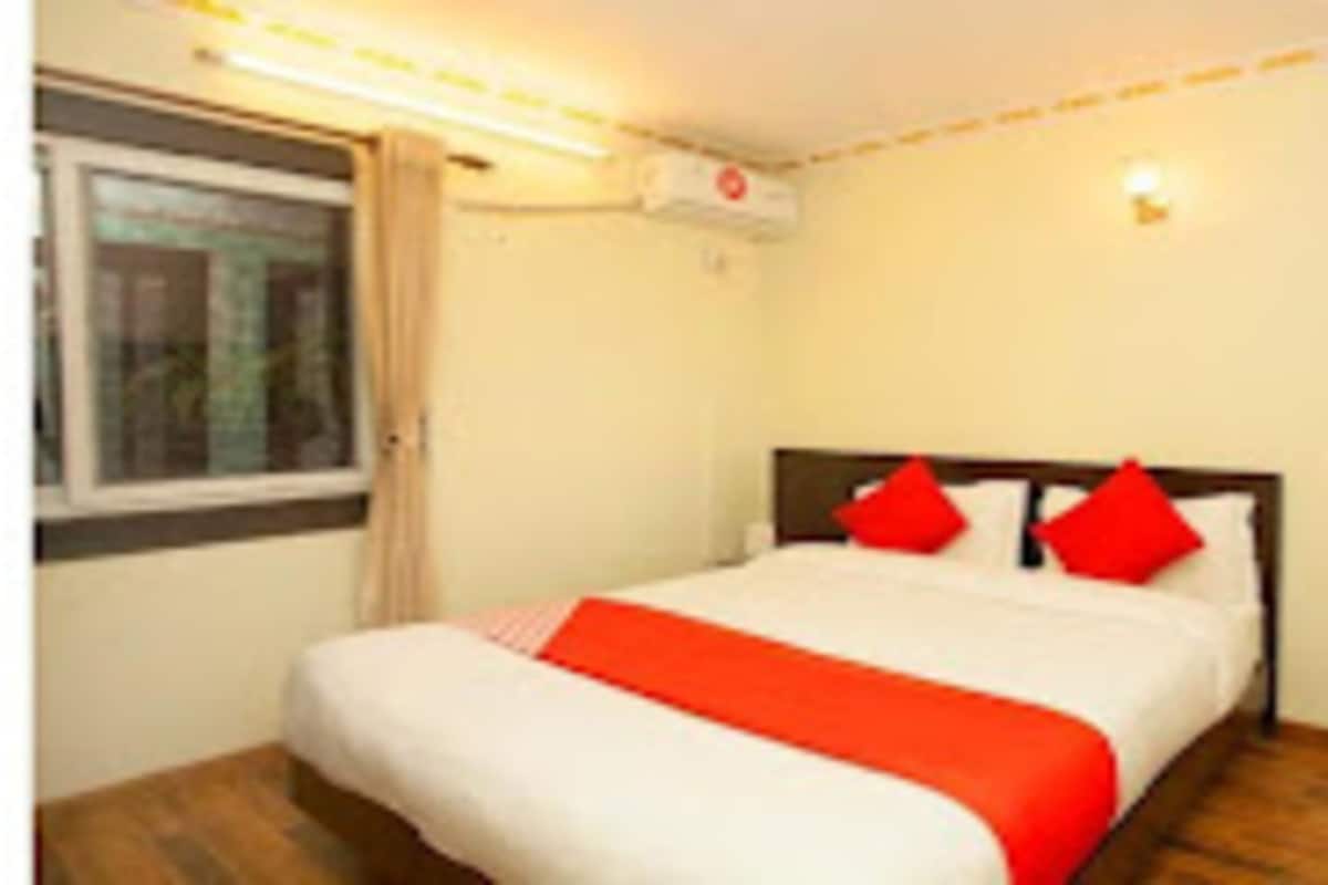 Una cama bien hecha con ropa de cama blanca y roja, una ventana con cortinas y una lámpara en el techo.