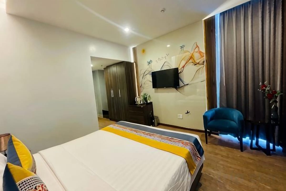 Una habitación de hotel con una cama, una silla, un televisor y un ventanal con cortinas.