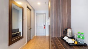 Un couloir avec un plancher en bois, un miroir, une porte et un plateau contenant des tasses et des bouteilles d’eau.