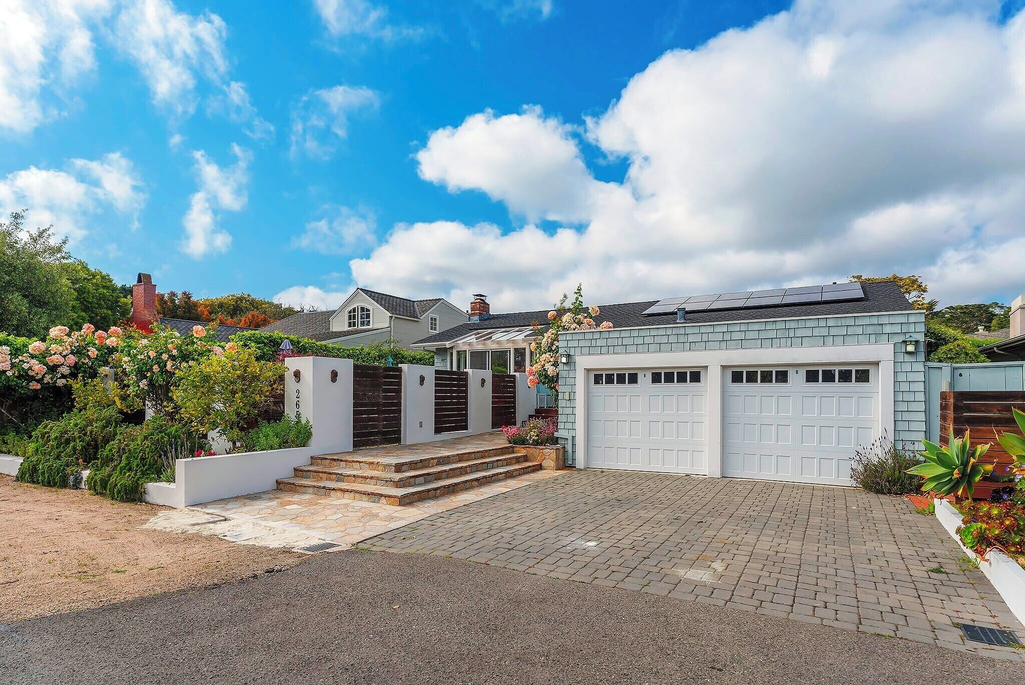 A modern house with a garage, a paved driveway, and a well-maintained garden with flowers.