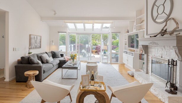 Ein geräumiges Wohnzimmer mit grauem Sofa, einem Holztisch und weißen Sesseln.