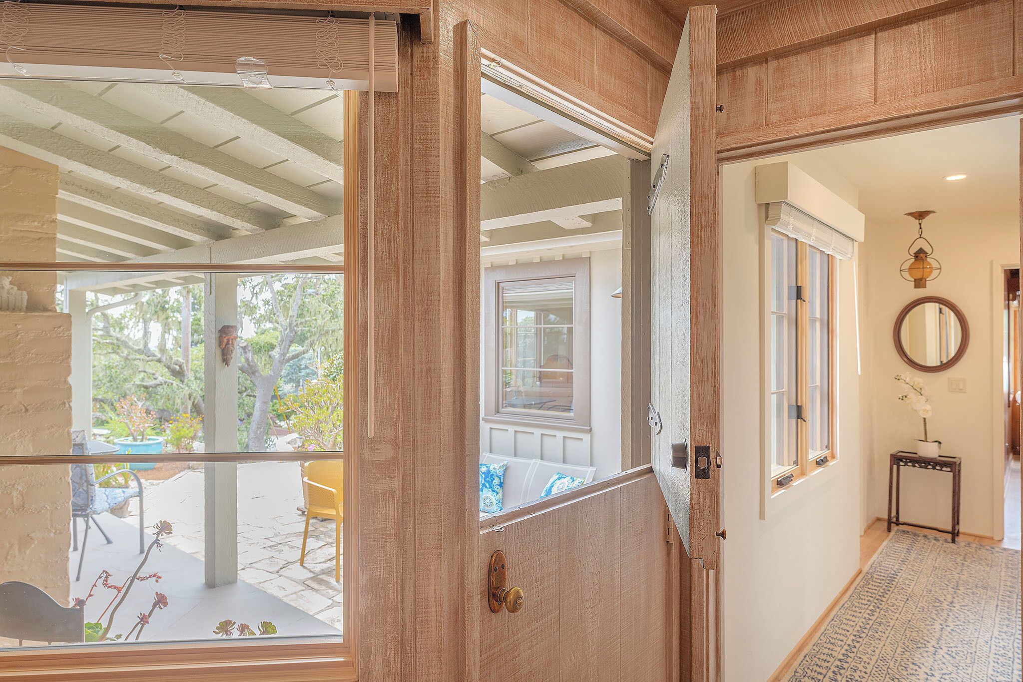 A wooden door leading to a covered patio area with a view of a garden.
