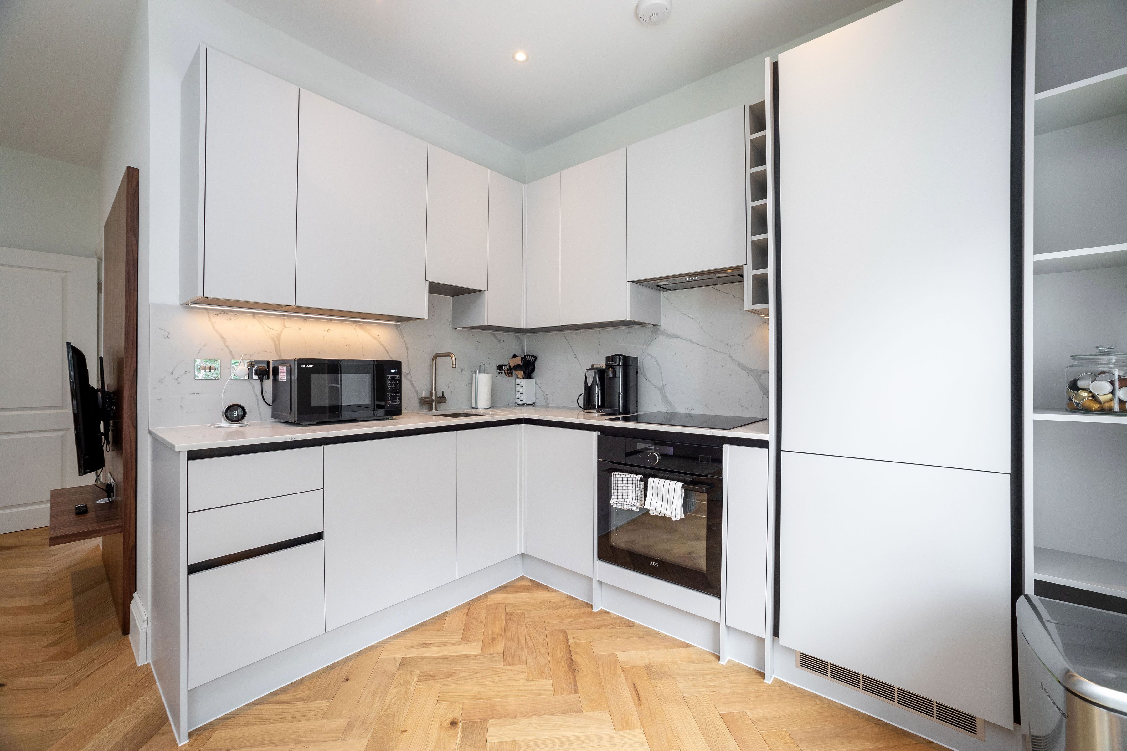 A modern kitchen with white cabinetry, a herringbone wood floor, a built-in oven, and a microwave.