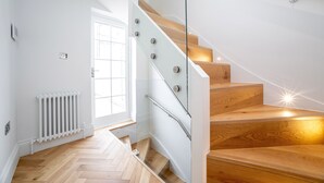 A modern staircase with glass railings and wooden steps, leading to a bright room with a white radiator and a window. - 3 Bedroom flat with Terrace in Central London (London)